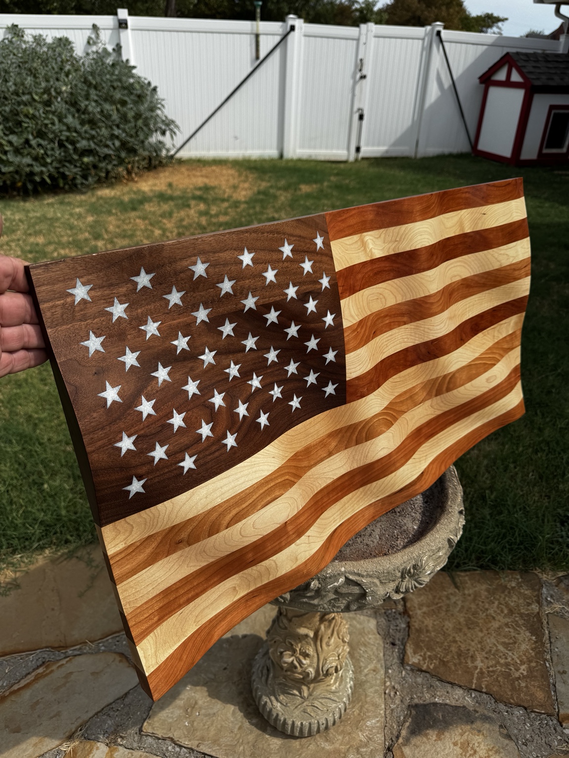 Completed wavy wooden flag photographed outdoors on a stone pedestal